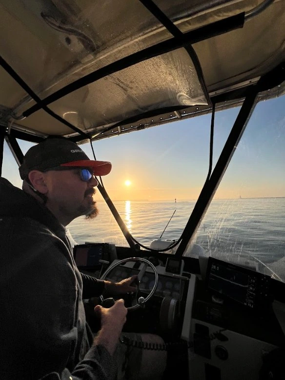 Captain steering the Mystic Queen sportfishing boat toward the fishing grounds at sunrise